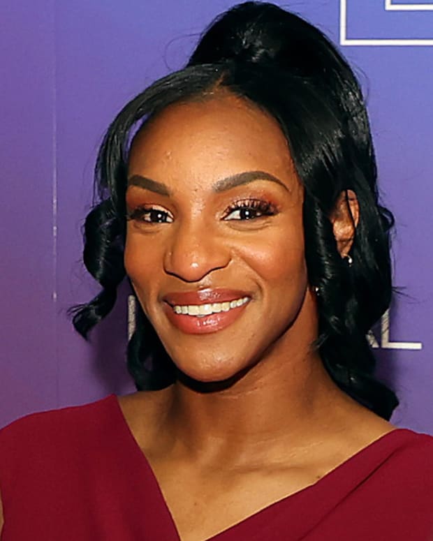 Crystal Dunn poses in a deep berry-colored V-neck top and a messy up-do and smiles for the camera.